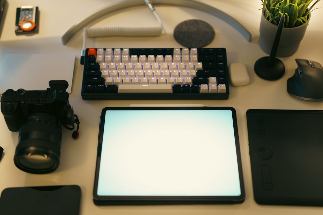 A stylish desk setup featuring a digital tablet, keyboard, camera, and plant, ideal for creative work.